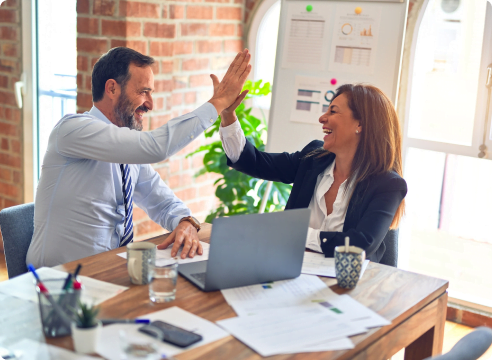 Woman and man high fiving over a laptop and paperwork